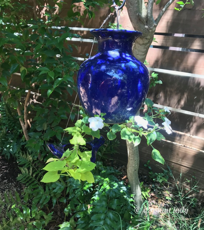 An upside down planter hangs from a tree with flowering impatiens. I don't know how the plant stays in without falling out, but it's cool!  Southwest garden style